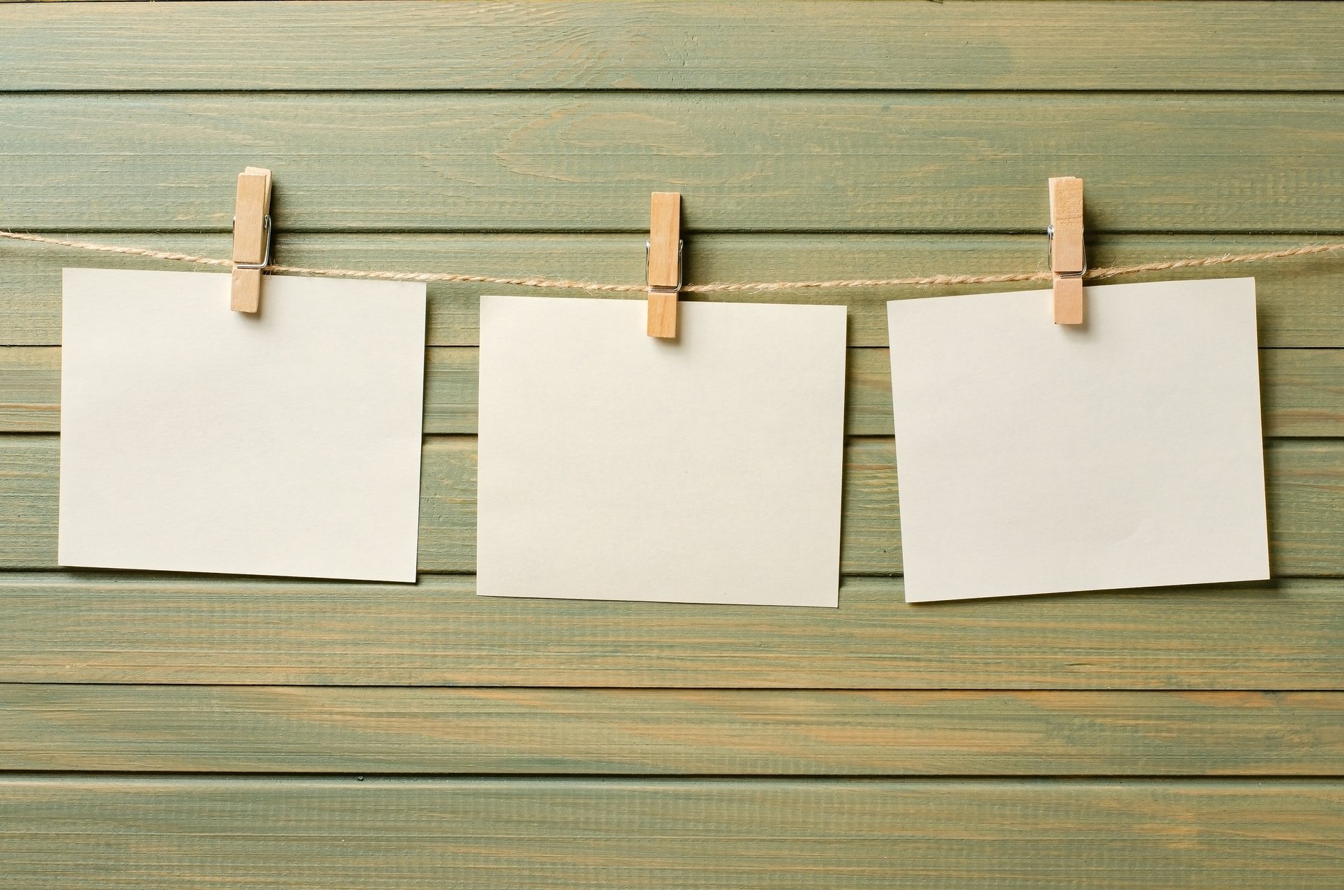 Empty paper sheets hang on a rope. A design element. Wooden background. Copy space.